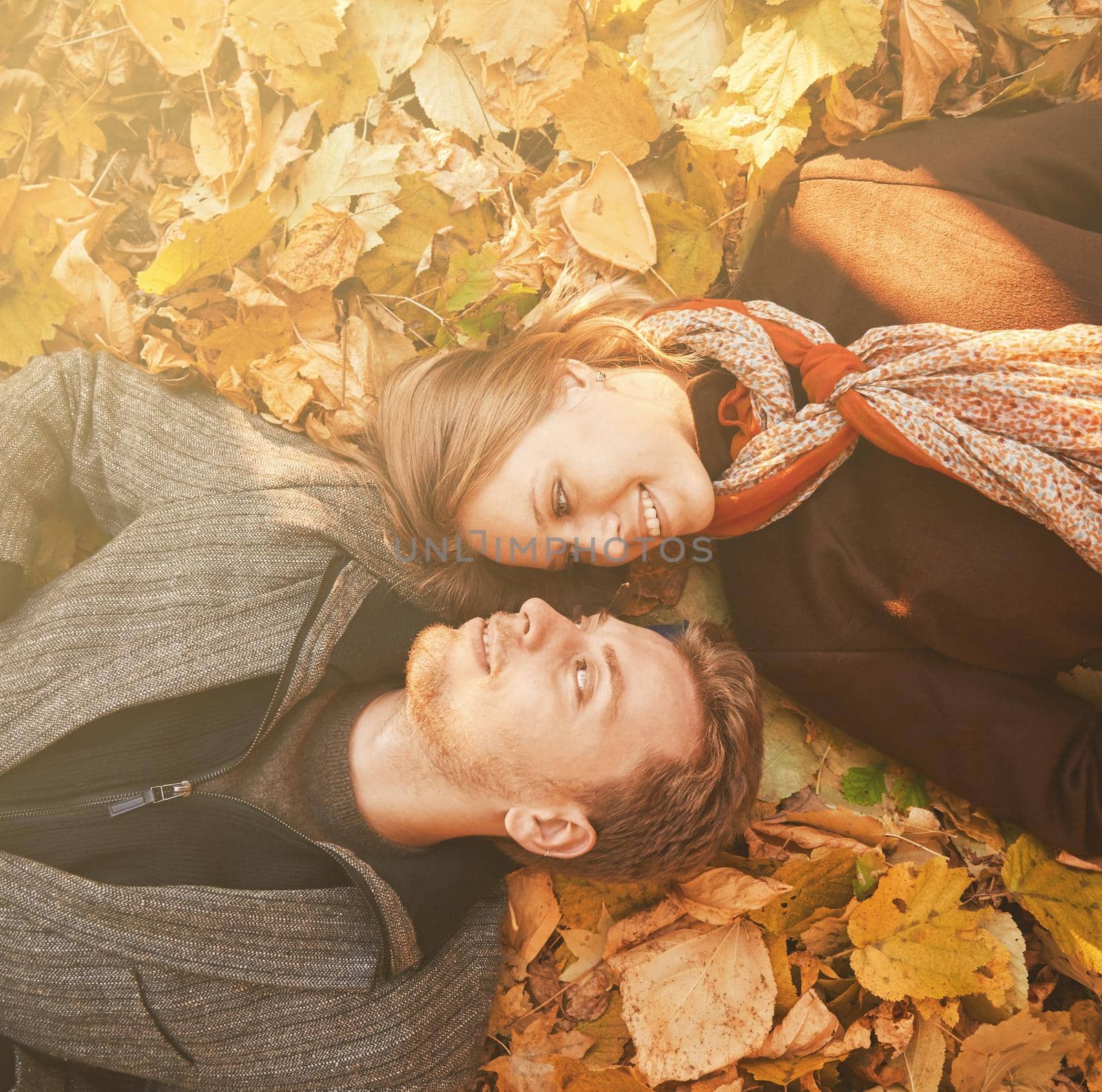 Happy loving couple lying on autumn leaves in the park, top view. Image with sunlight effect.