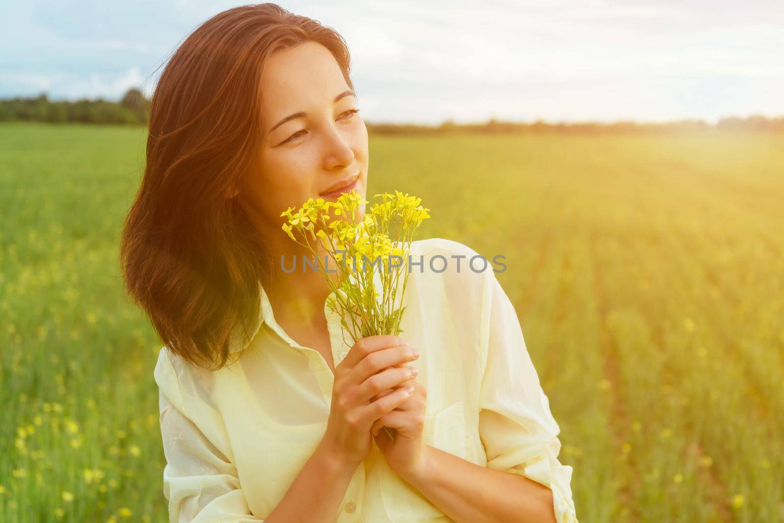 Smiling beautiful young woman holding bouquet of yellow flowers in summer outdoor. Image with sunlight effect