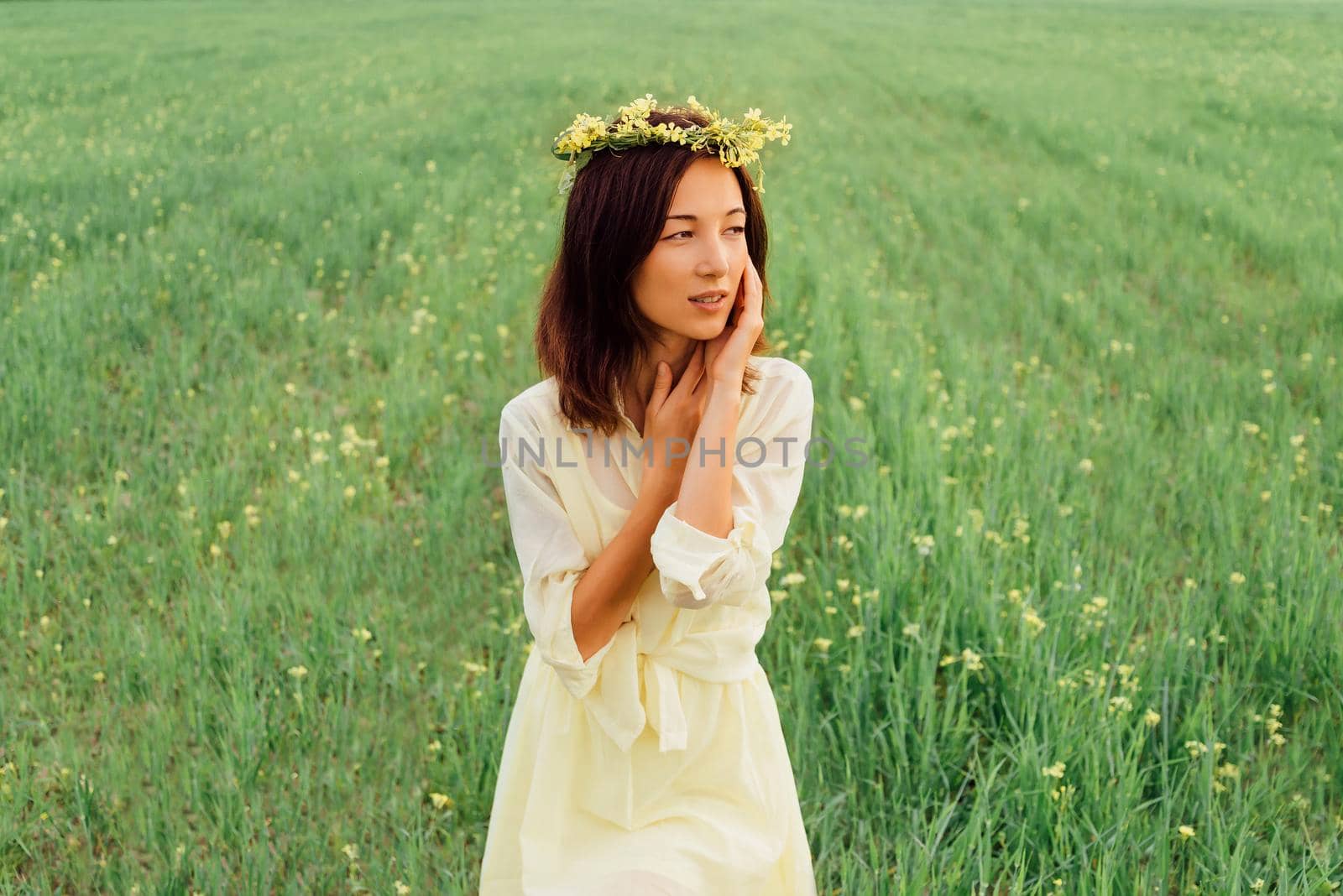 Beautiful brunette young woman with wreath of flowers resting on summer meadow
