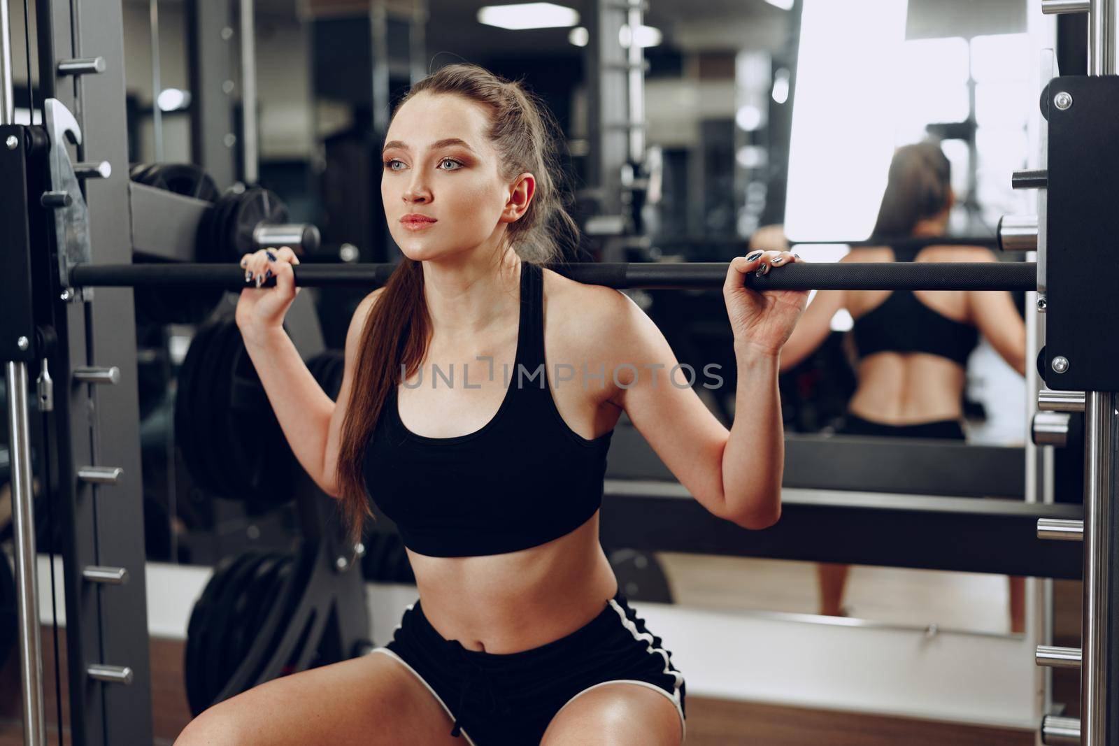 Young woman doing squats with barbell in a gym apparatus close up