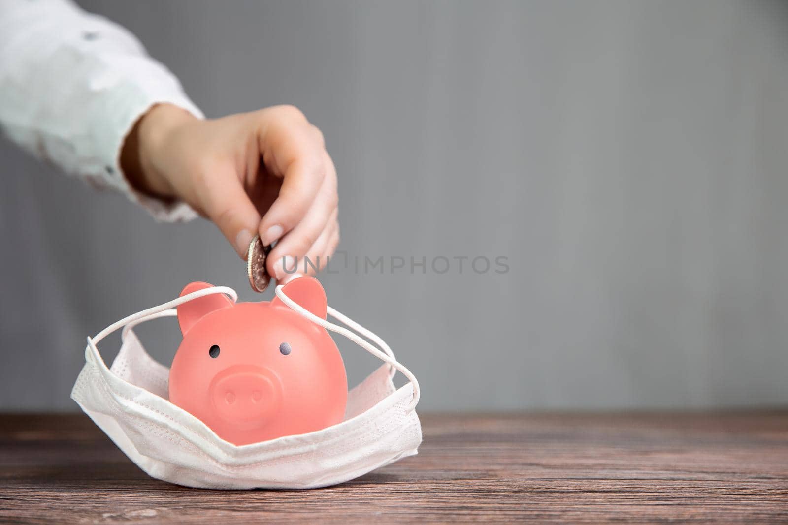 Inserting coin in piggy bank for savings with protective medical mask for pandemic, virus Covid-19, coronavirus,business,fianancial,saving concepy with copy space space for tect