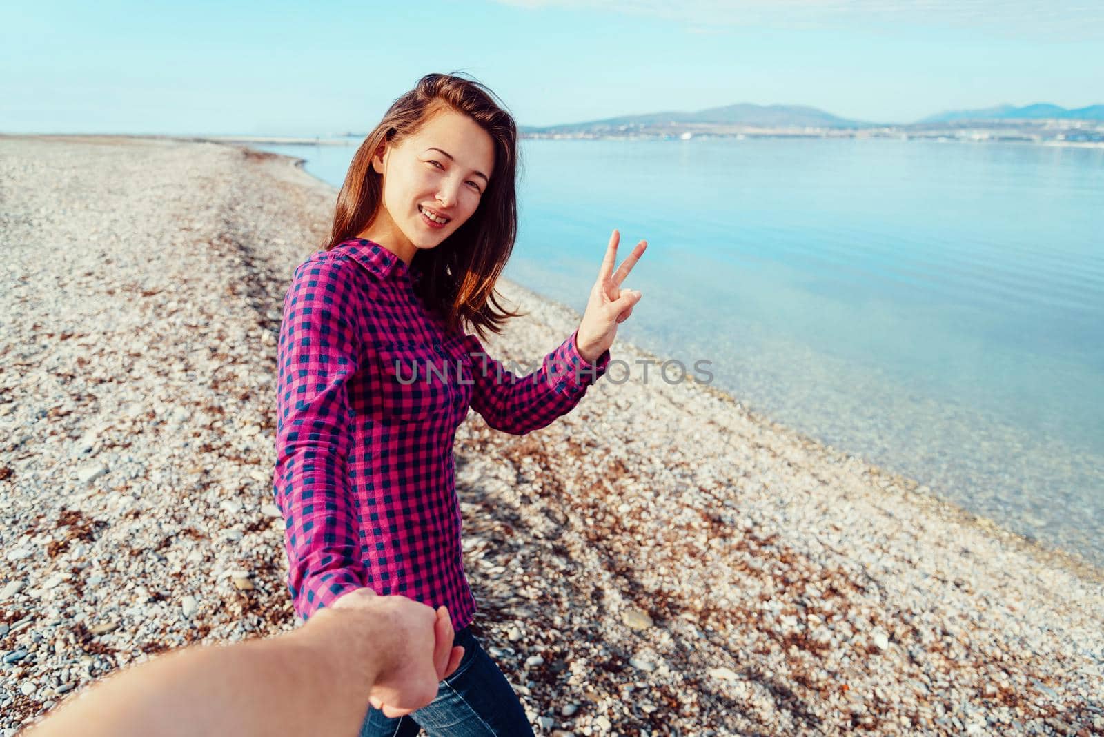 Couple in love. Smiling young woman holding man's hand and showing peace sign on beach near the sea