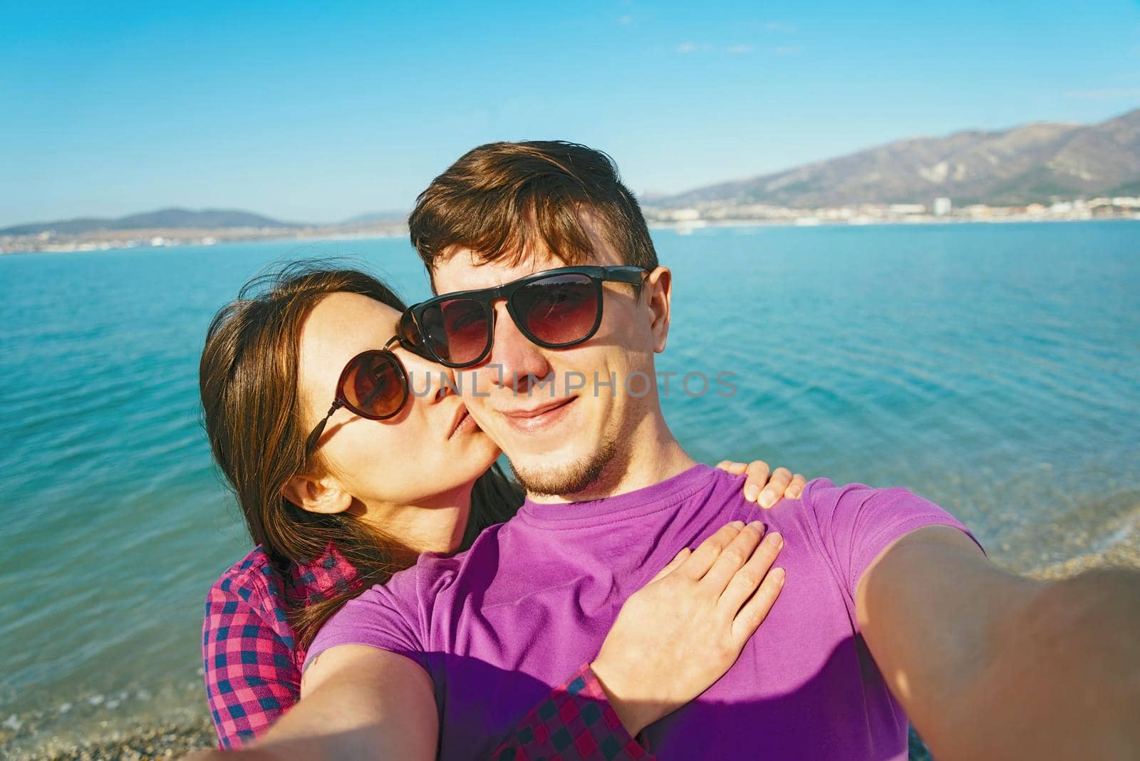 Happy young couple in love taking self-portrait on background of blue sea and woman kissing a man