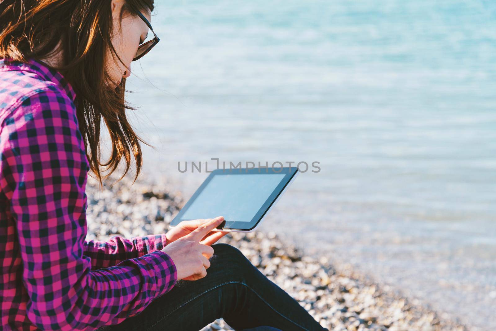 Young woman sitting on beach near the sea and working on digital tablet. Focus on face