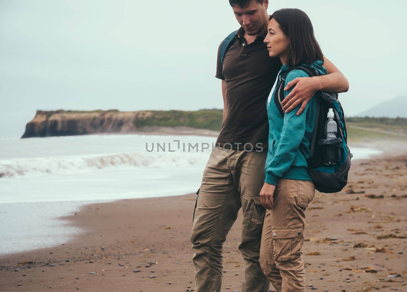Traveler couple in love with backpacks walking on beach near the sea in summer. Man embracing a woman