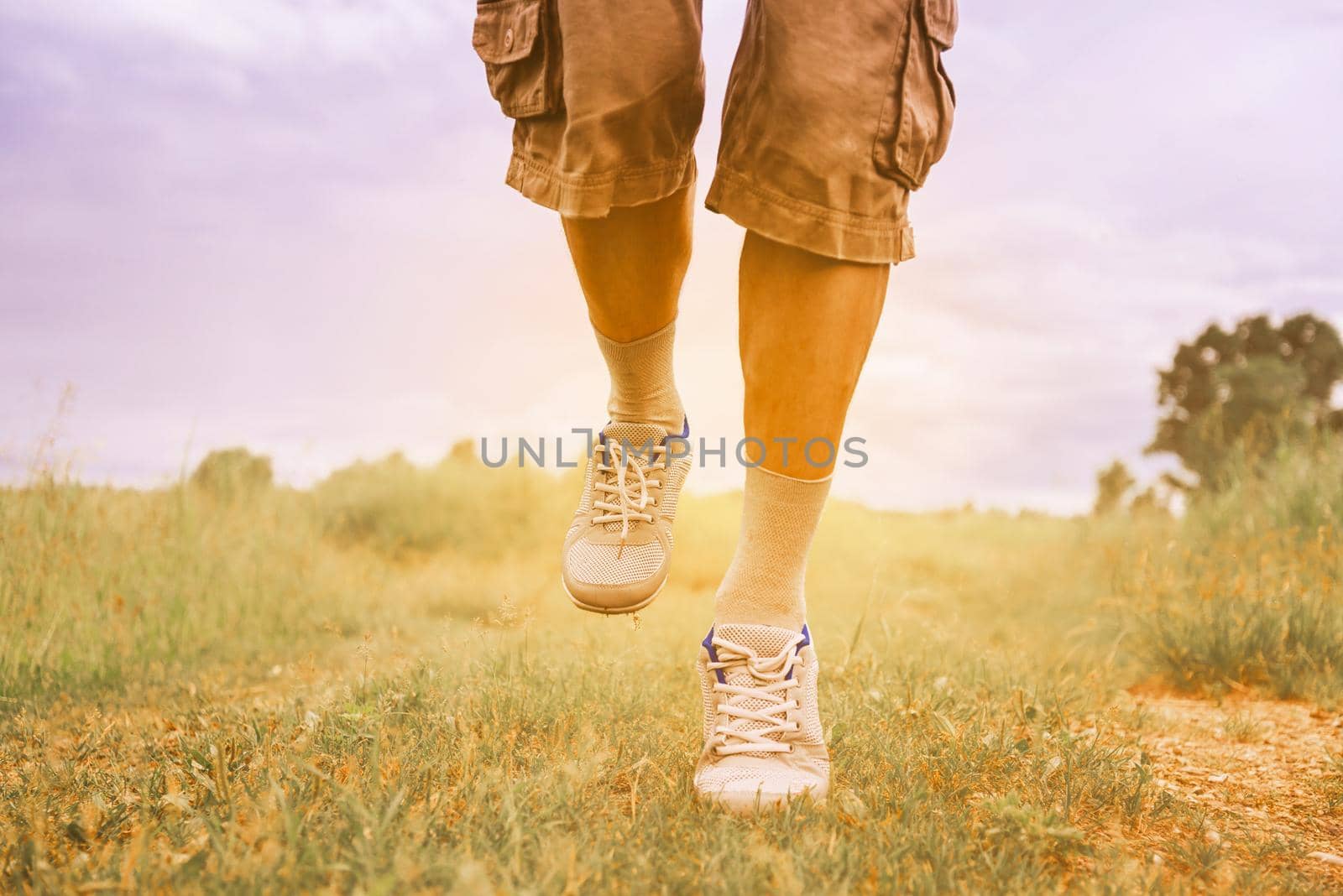 Unrecognizable man running on footpath in summer, view of legs. Image with sunlight effect. Theme of sport and healthy lifestyle