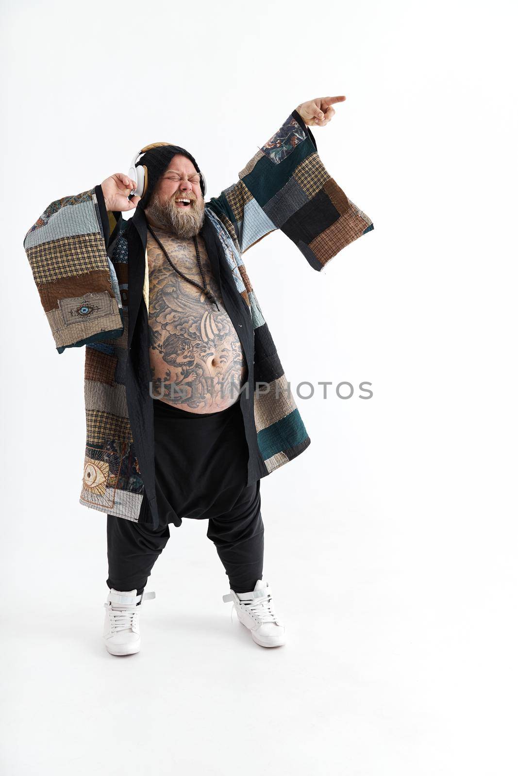 Fat stylish bearded tattoed caucasian man with big belly is posing and dancing wearing ethnic kimono