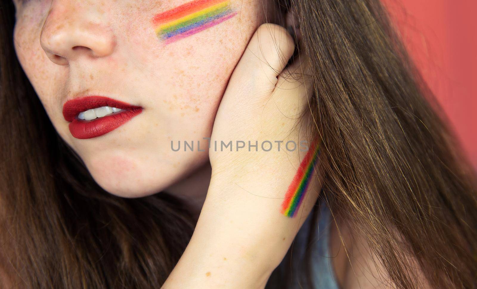 Portrait of a young woman with rainbow Flag on cheek and body, the LGBT community on a colorful pink background freedom, LGBTQ concept beauty