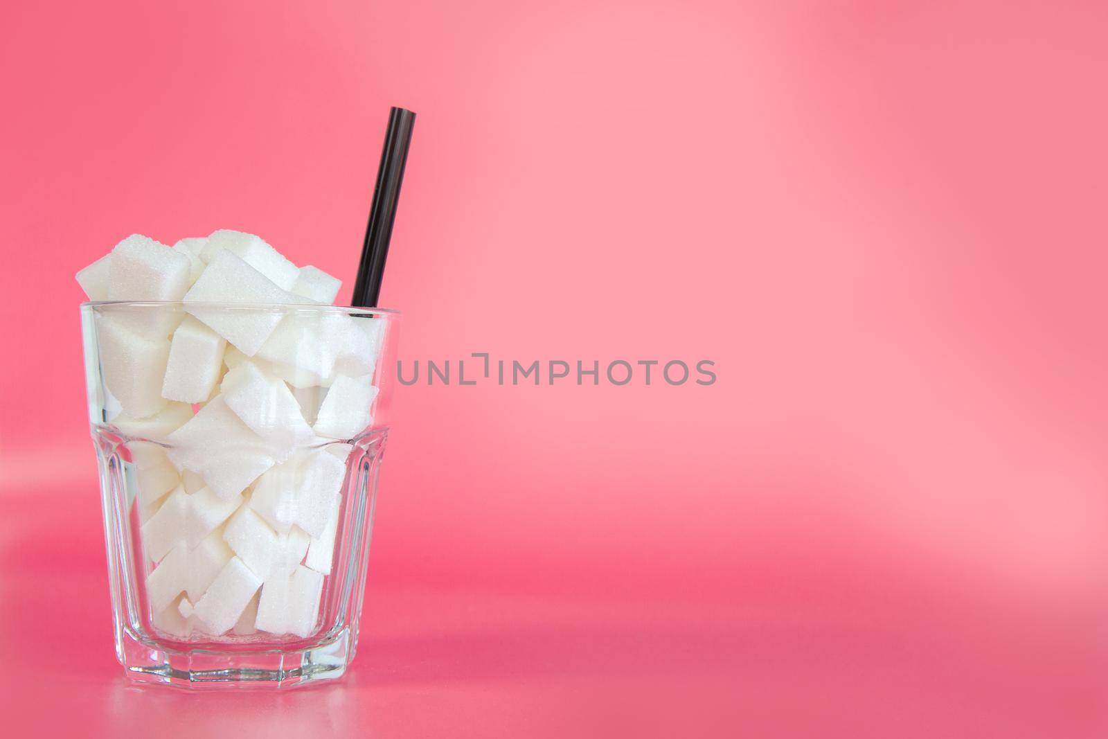 Glass full with sugar cubes with straw on pastel pink and blue background with copy space, retro design, Sweets,candy,soda,unhealthy eating concept. modern design colorful