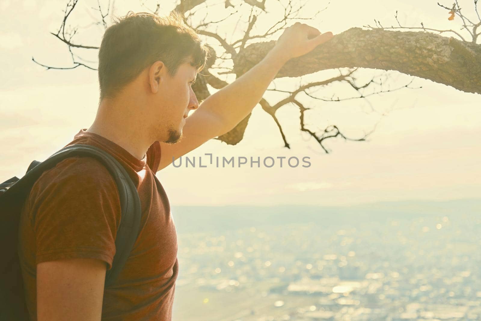 Traveler young man with backpack looking at the city from hill. Concept of tranquil life from the urban bustle. Image with sunlight effect