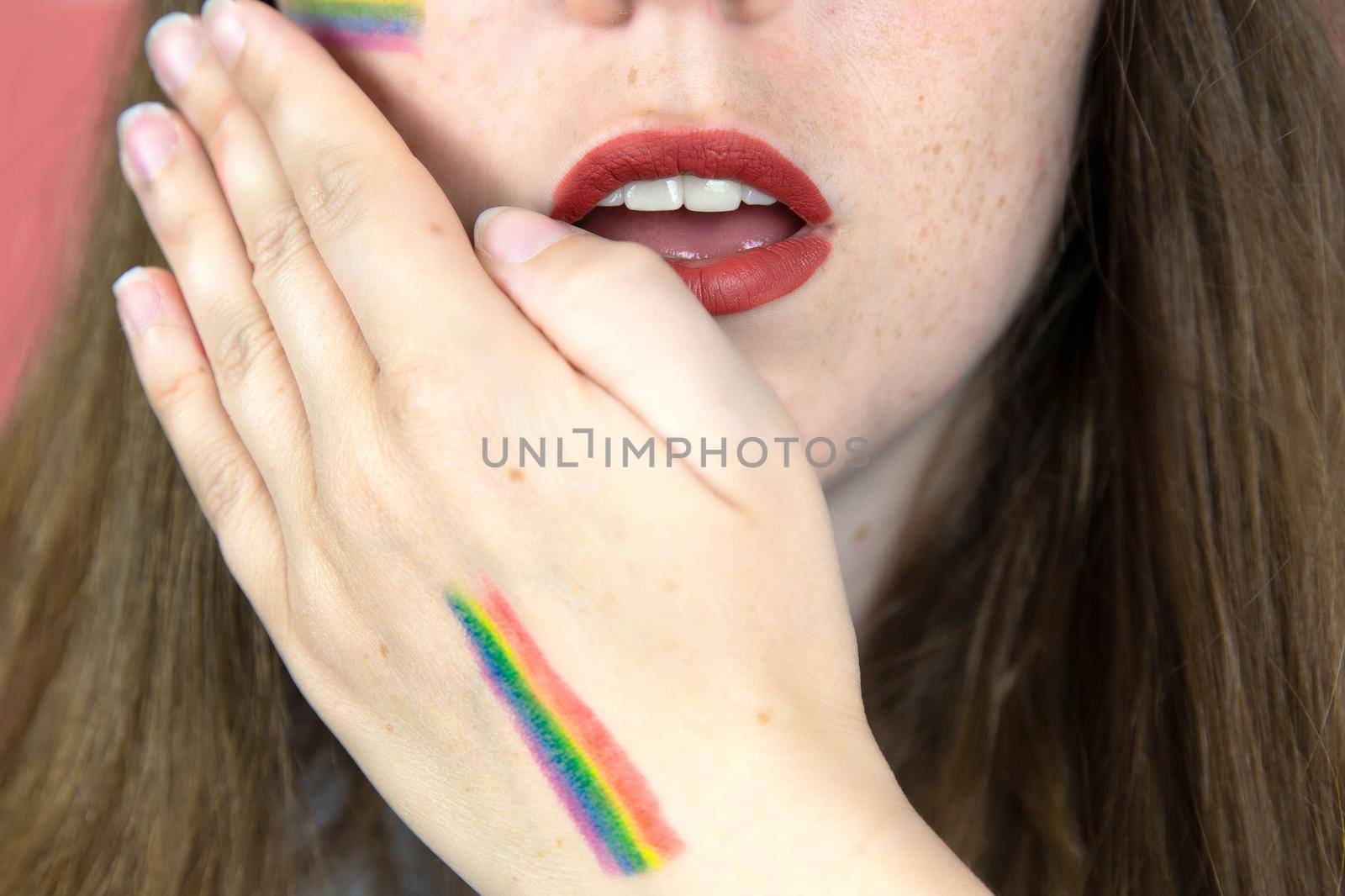 Portrait of a young woman with rainbow Flag on cheek and body, the LGBT community on a colorful pink background by Annebel146