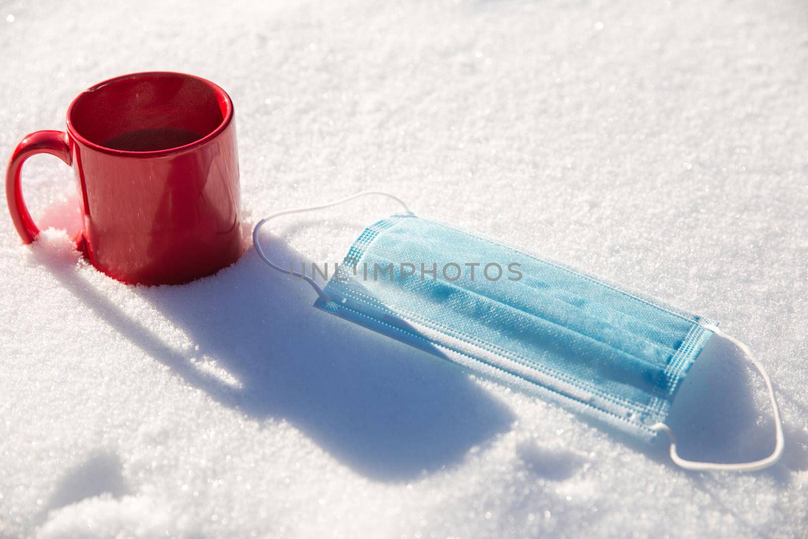 Red mug with hot coffee,tea or chocolate milk and protective blue medical mask for coronavirus Covid-19 pandemic. lies in the snow, Winter,virus,drink and health concept background beauty