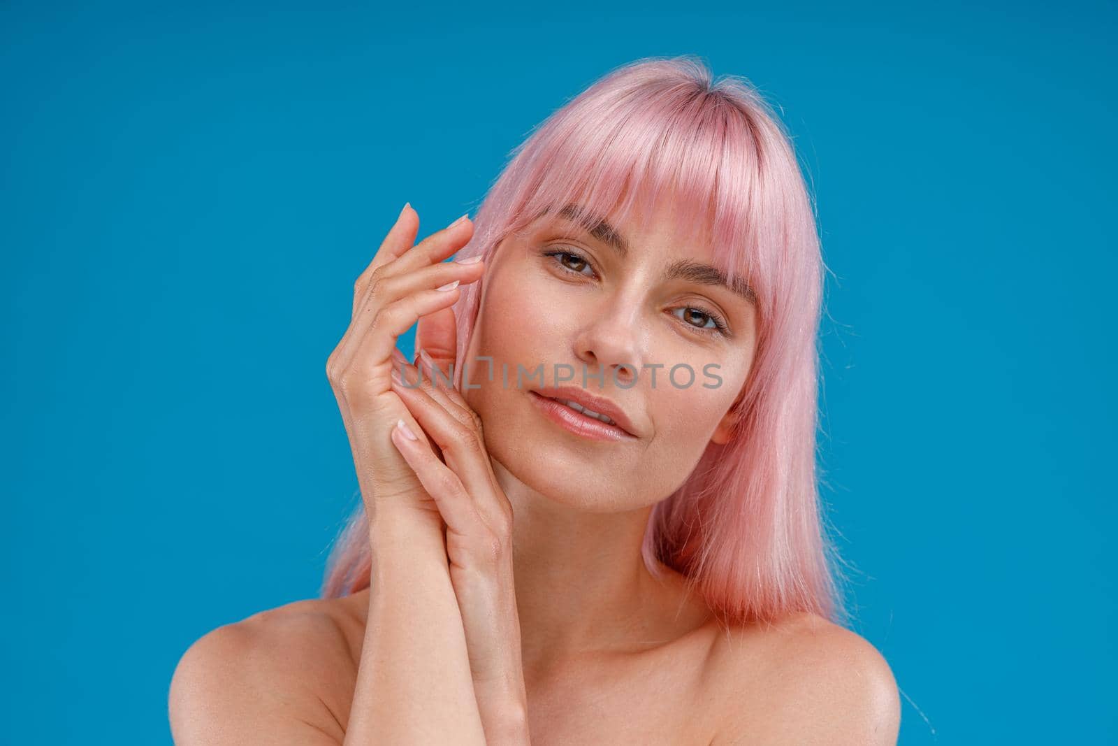 Sensual naked woman with pink hair and perfect glowing skin looking at camera, posing isolated over blue studio background by Yaroslav_astakhov