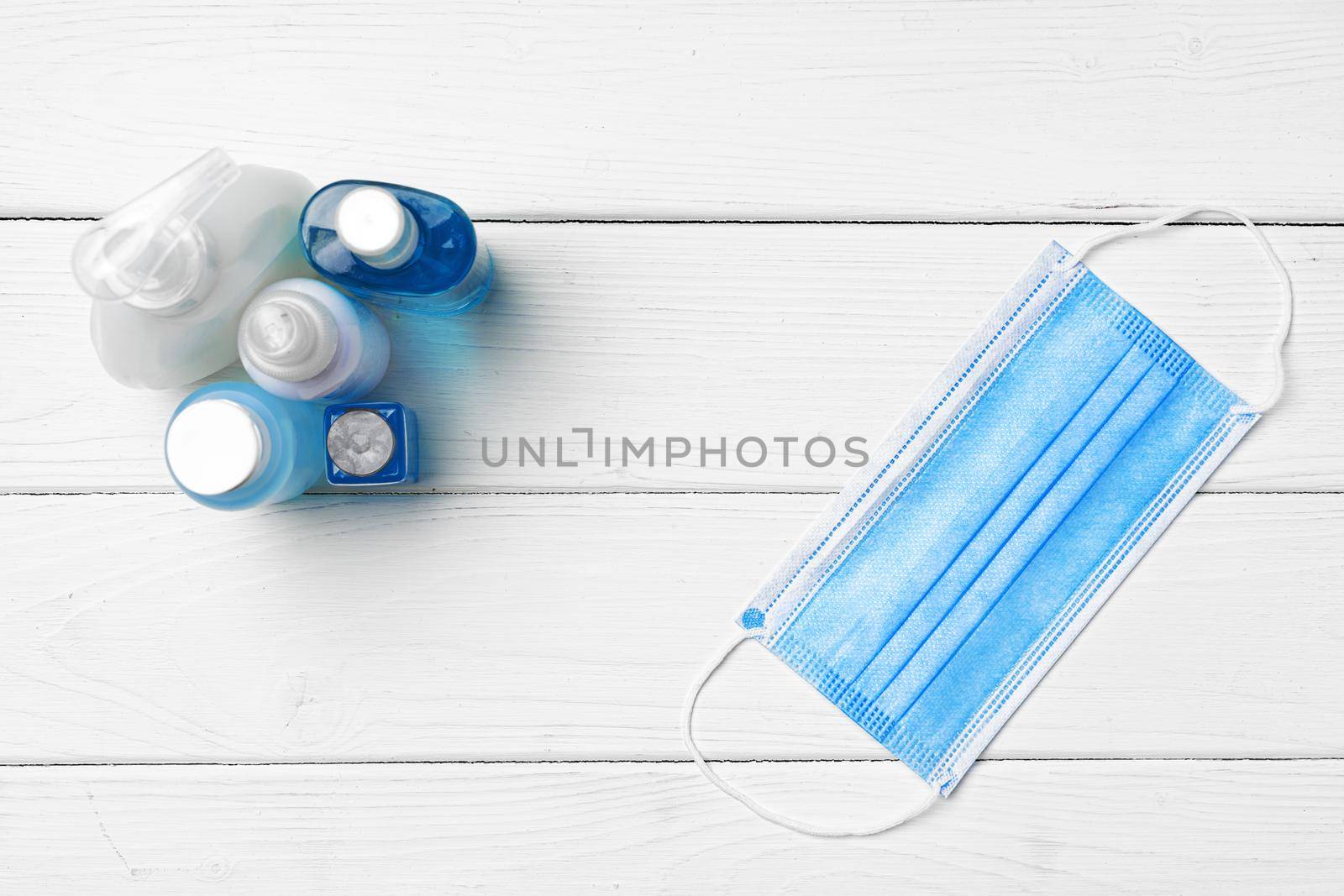 Medical face mask and sanitizer gel on white wooden background close up