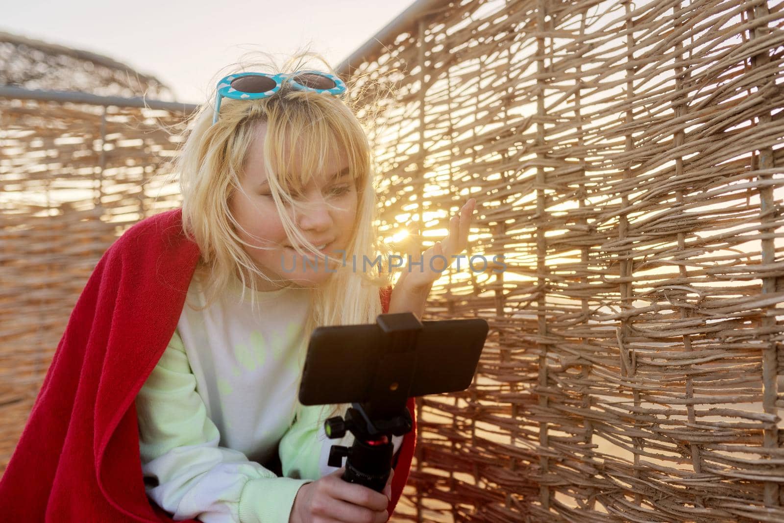 Outdoor sunset portrait of female teenager recording video on smartphone by VH-studio