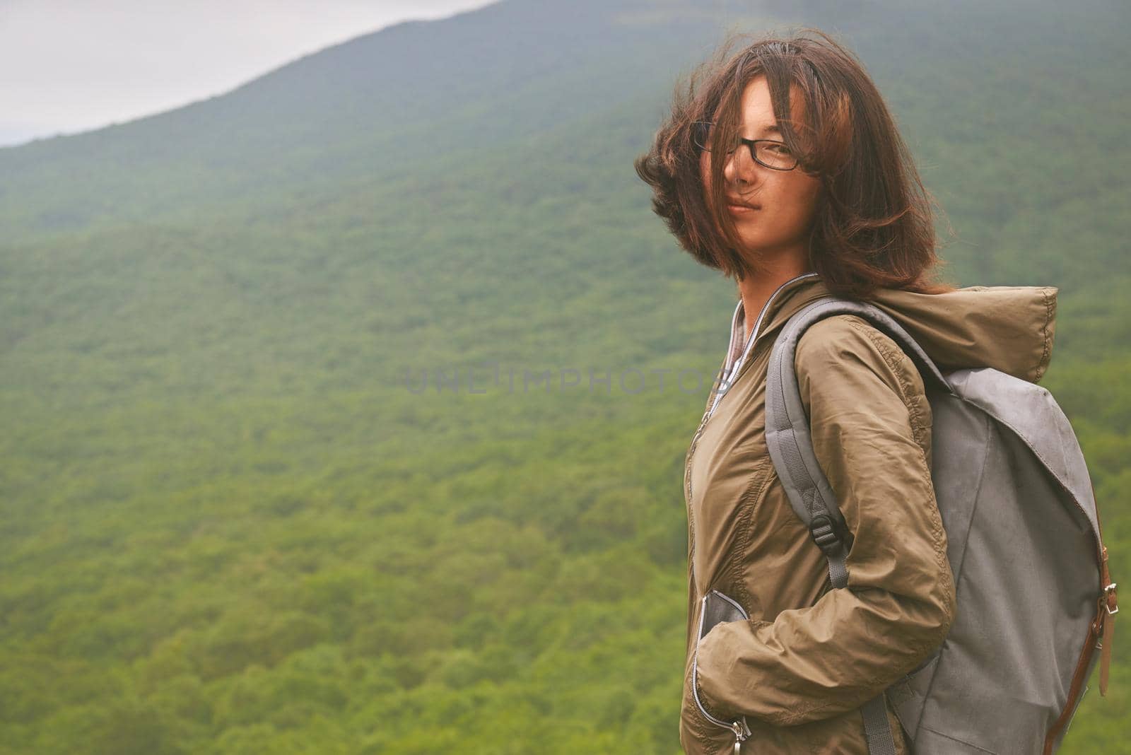 Hiker young woman standing on background of the mountain in summer and looking into the camera
