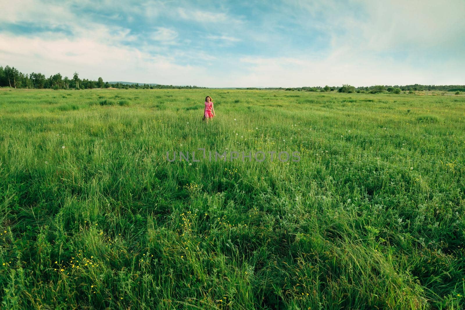 Happy little girl in pink dress walking on summer green meadow