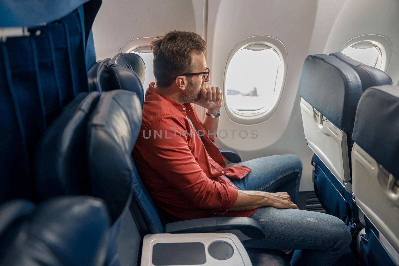 Pensive caucasian man in casual wear resting on the plane, sitting and looking out the window by Yaroslav_astakhov