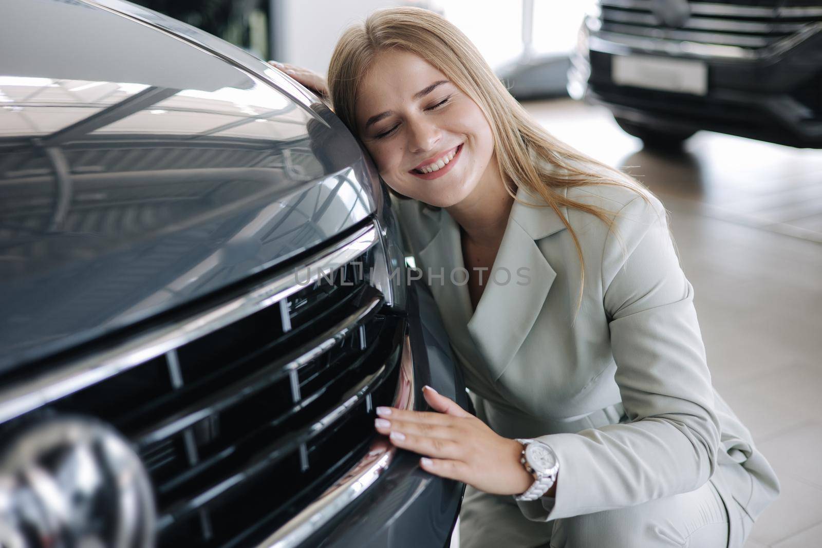 Business woman chossing a new car in a car showroom. Happy female hug new car and very glad by Gritsiv