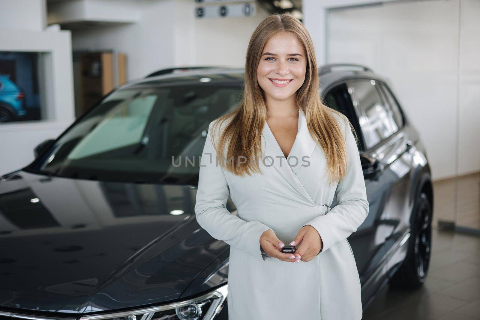 Portrait of beautiful and young business woman in car showroom. Female hold keys from mher new car.