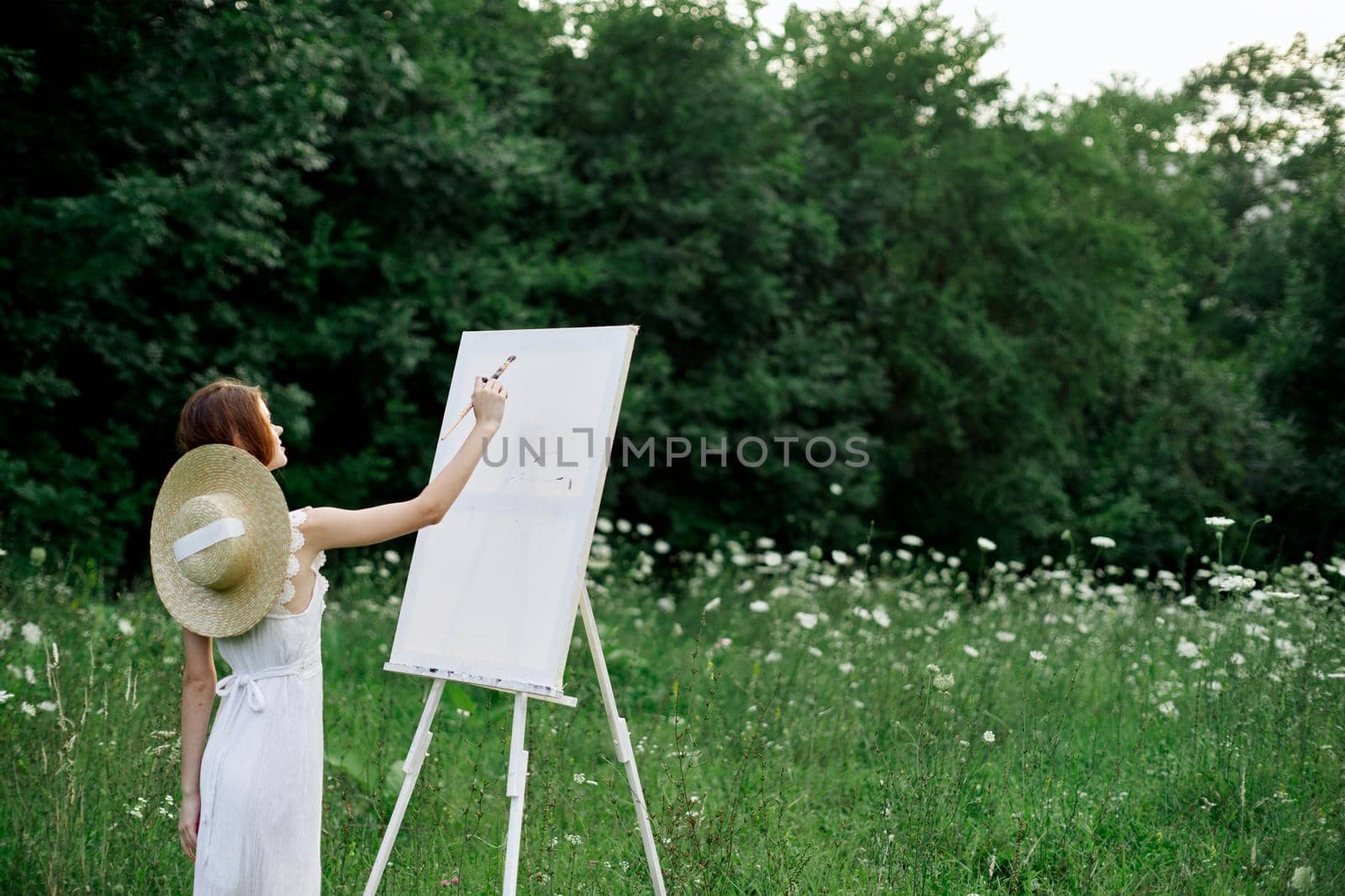 Woman in white dress paints a picture outdoors hobby creative. High quality photo