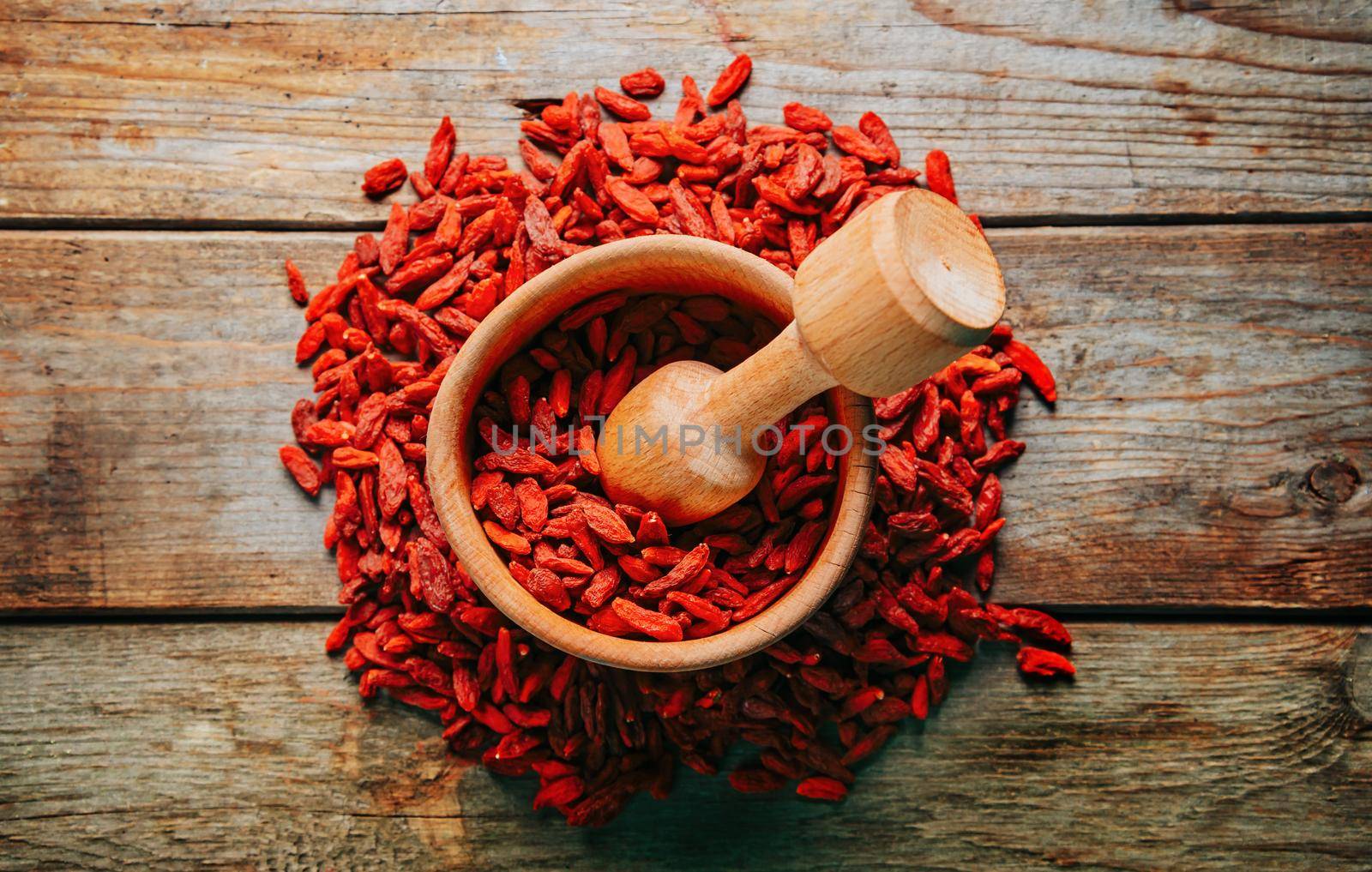 Goji berries in mortar with pestle on wooden background, top view