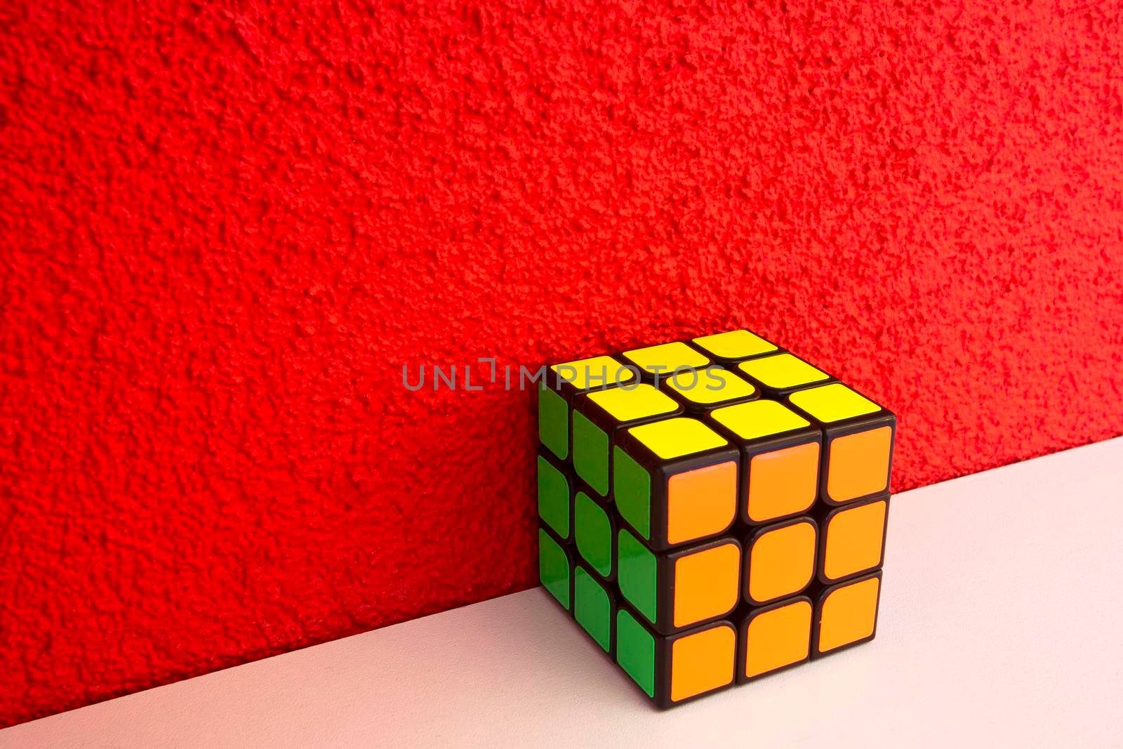 Solved puzzle speed cube on white wooden shelf near red colored wall, colorful rubiks cube with copy space mind challanging retro design