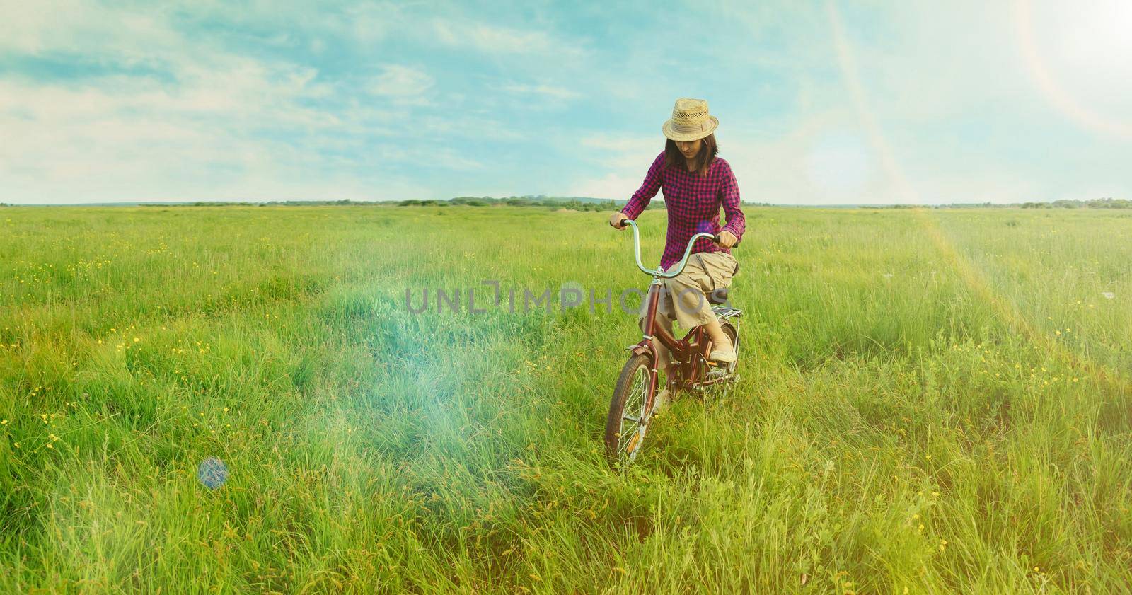 Hipster young woman cycling on green meadow in summer. Image with sunlight effect