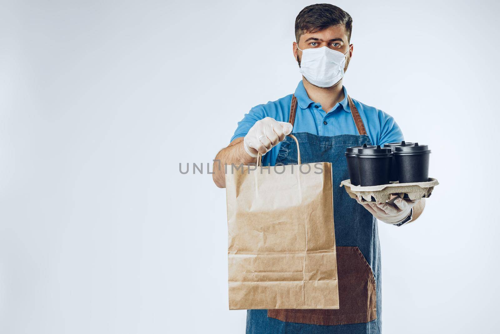 Delivery man in protective mask and medical gloves holding takeaway food. Compliance with the hygiene rules while covid-19 pandemic. Safe service