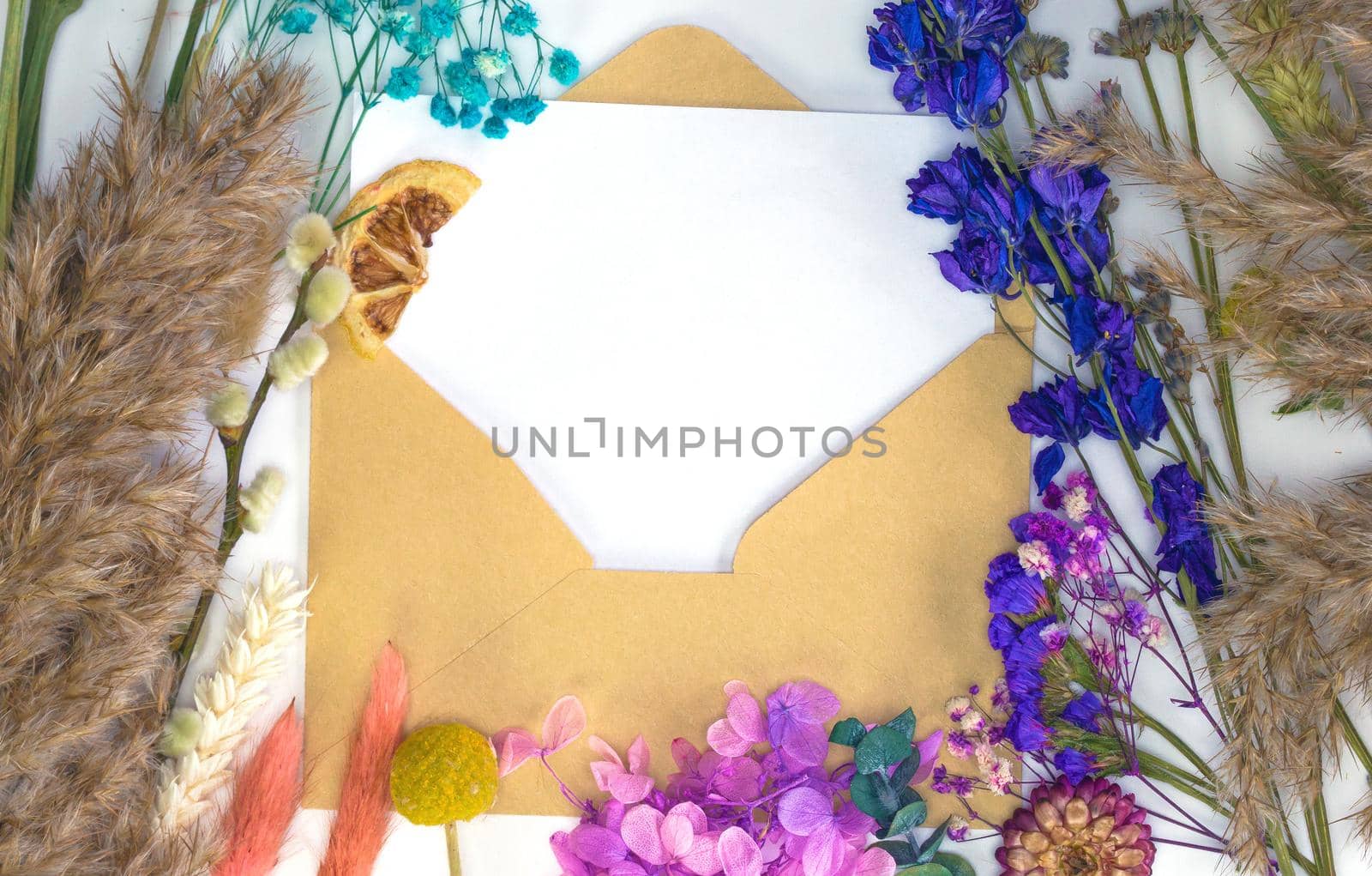 Blank white paper with craft paper envelope and colorful dried spring flowers and reed , blossom, flat lay, top view modern background, design,greeting card, copy space