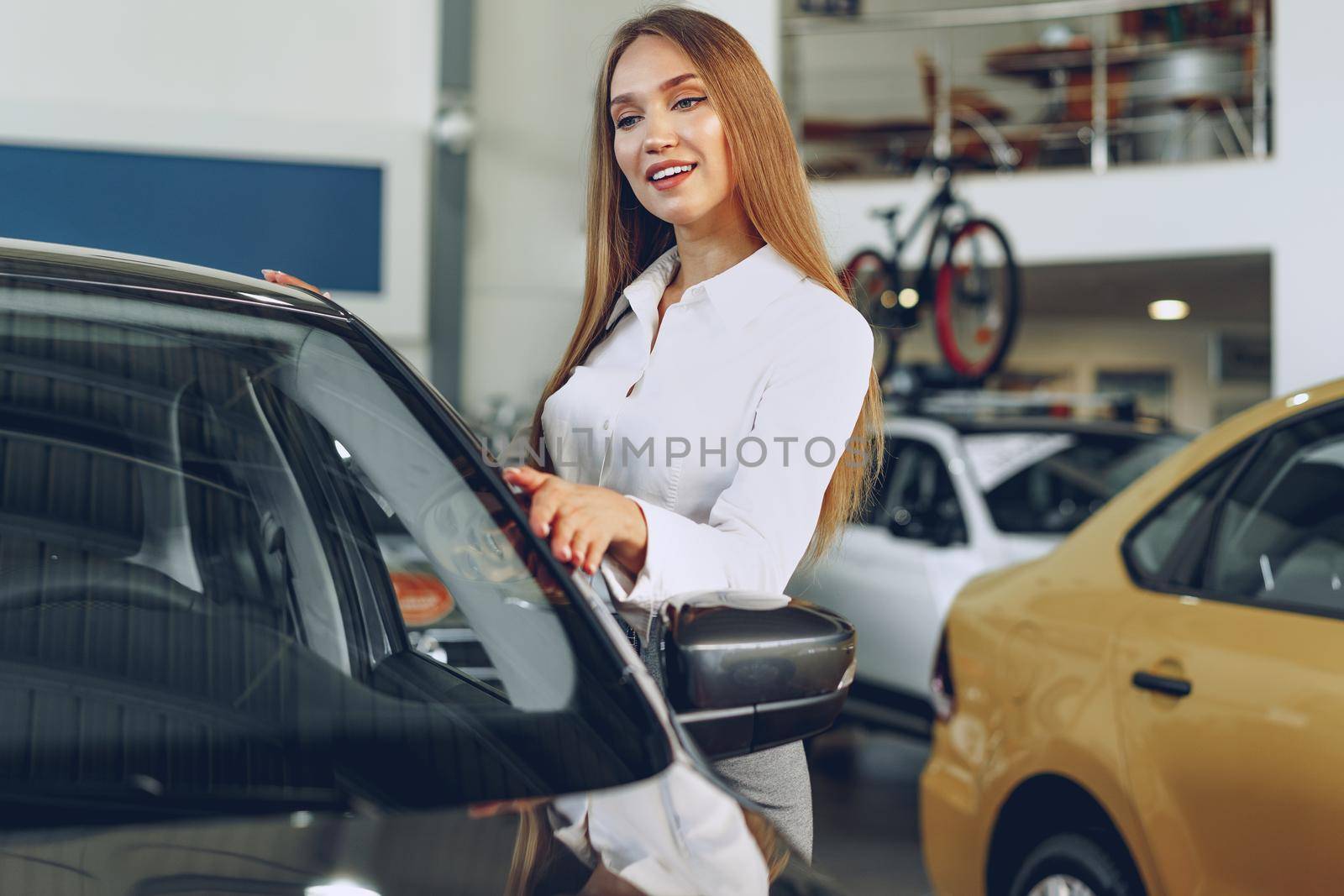 Beautiful young woman touching her new car with pleasure and joy