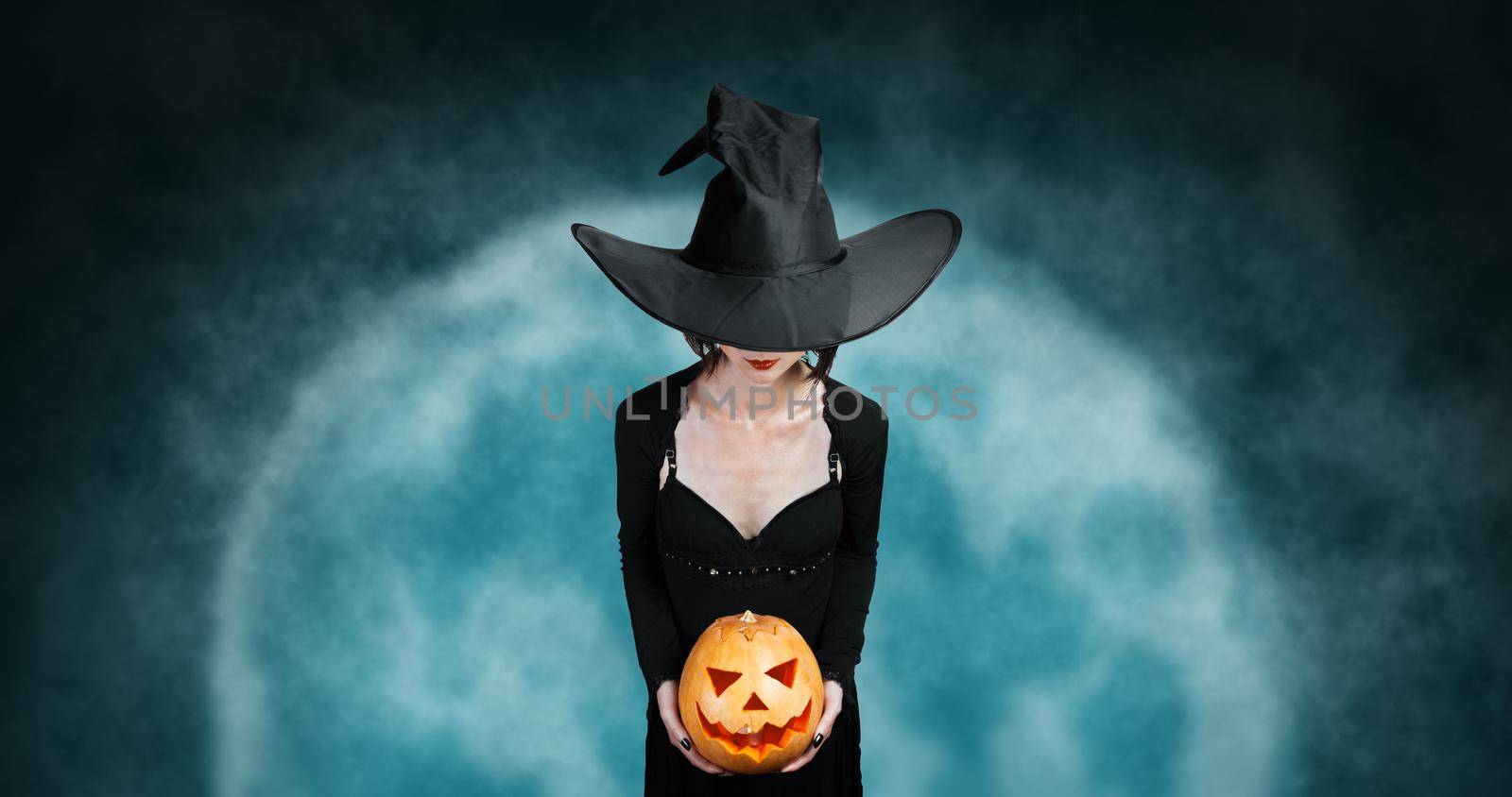Witch holds Halloween carved pumpkin on background of full moon. Halloween, horror theme