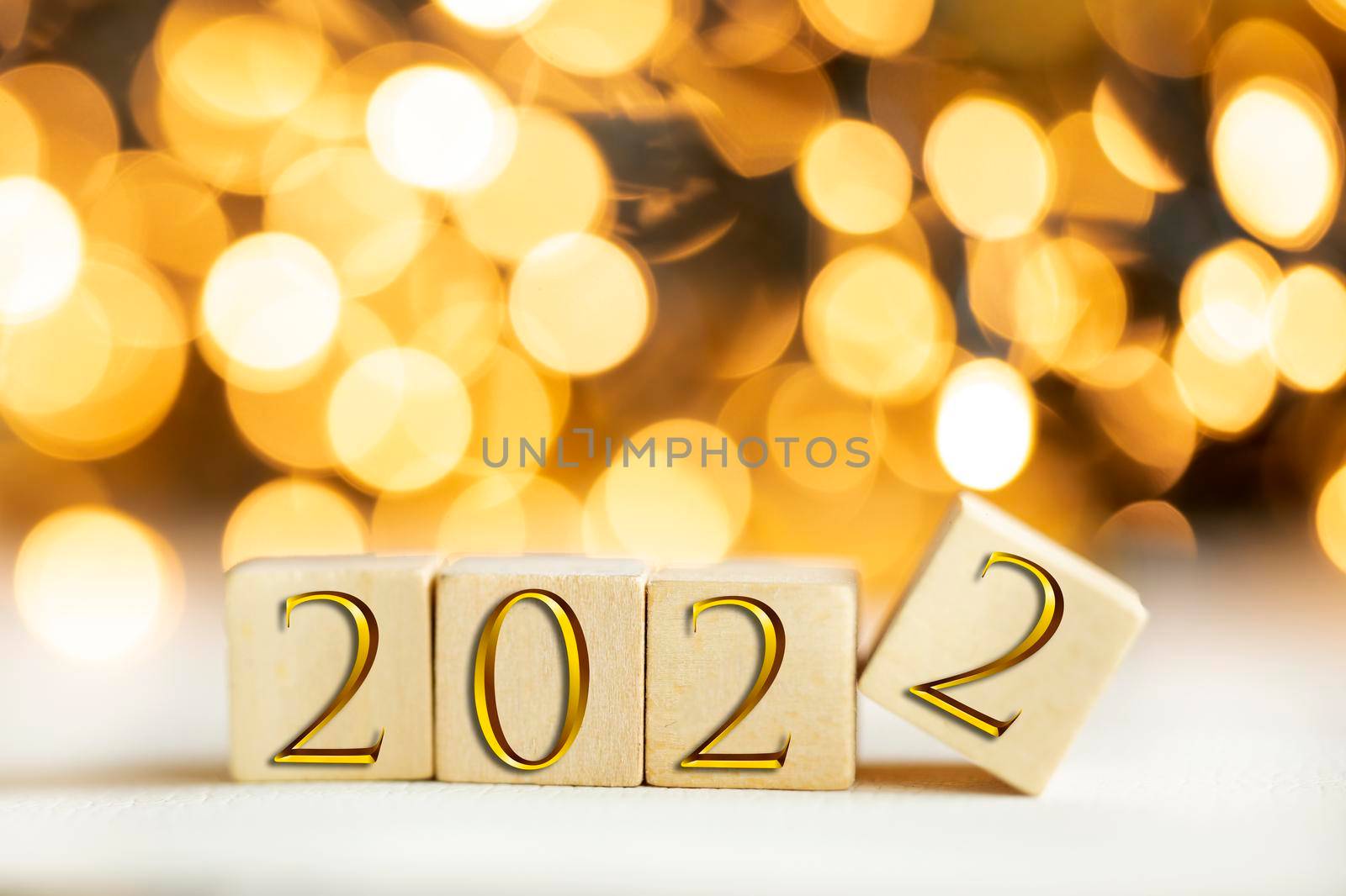 The year 2022 written on wooden cubes in gold luxury letters with shiny bokeh background, New Year celebration concept glitter beauty