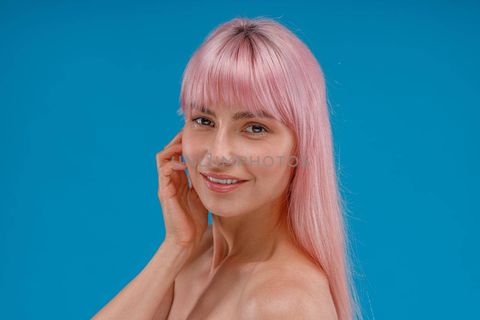 Portrait of beautiful young woman with pink hair and perfect skin smiling at camera, posing isolated over blue studio background by Yaroslav_astakhov