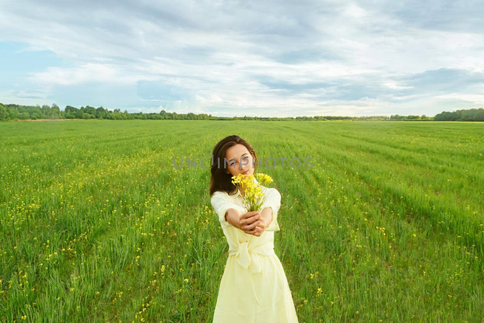 Beautiful young woman holding bouquet of yellow flowers on summer meadow