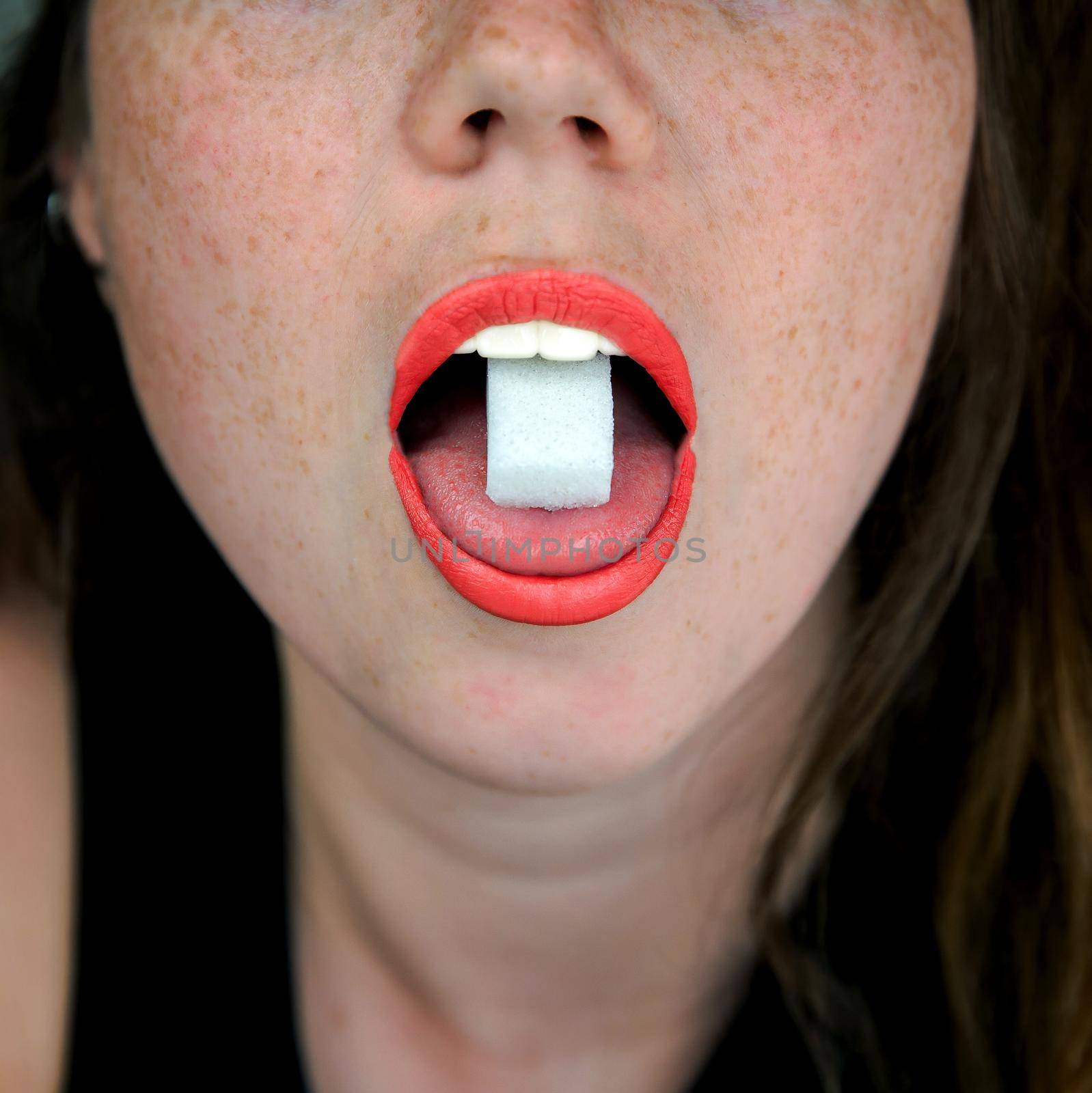 Close up of a woman with a sugar cube on her tongue in her mouth, unhealthy food,candy,sweets concept close up