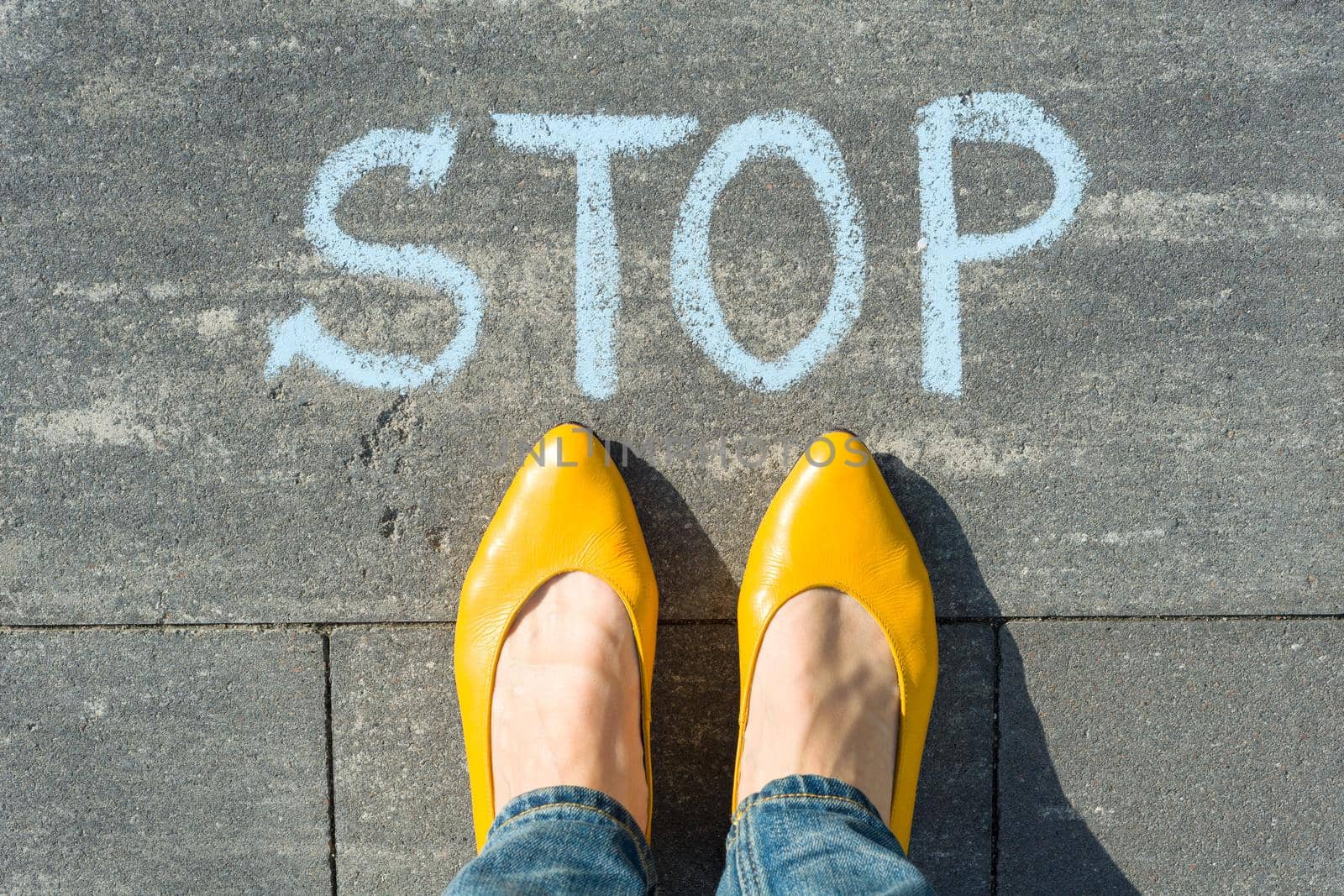 Female feet with text stop written on asphalt.