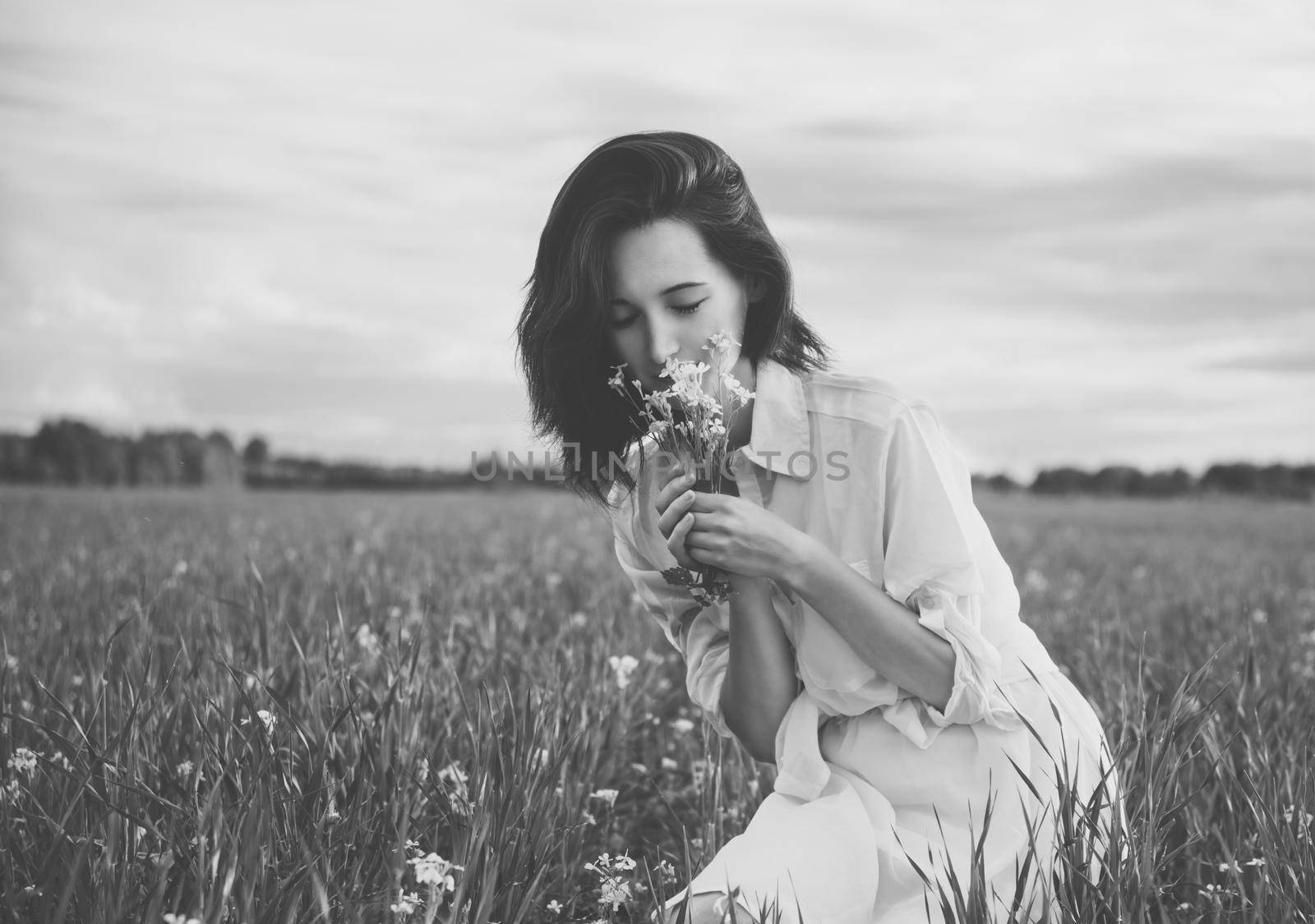 Young beautiful woman picking flowers in a summer meadow. With film grain and low contrast effect. Black-white photo.