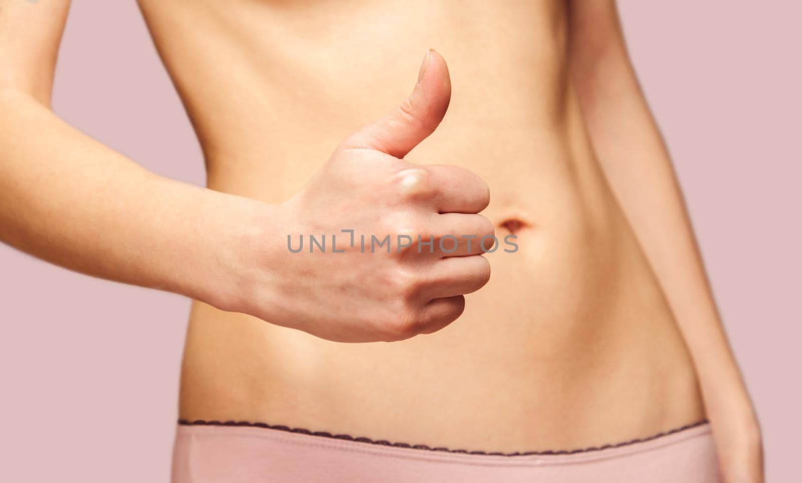 Unrecognizable woman is showing gesture thumb up in front of her slim belly