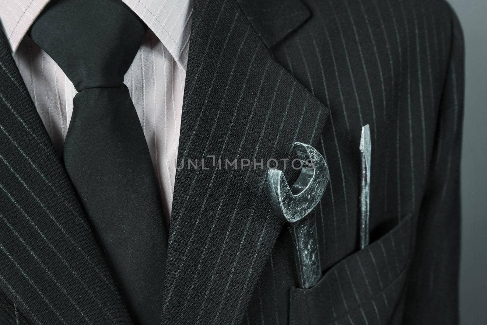 Close-up image of wrench and screwdriver in a pocket of suit businessman, face is not visible