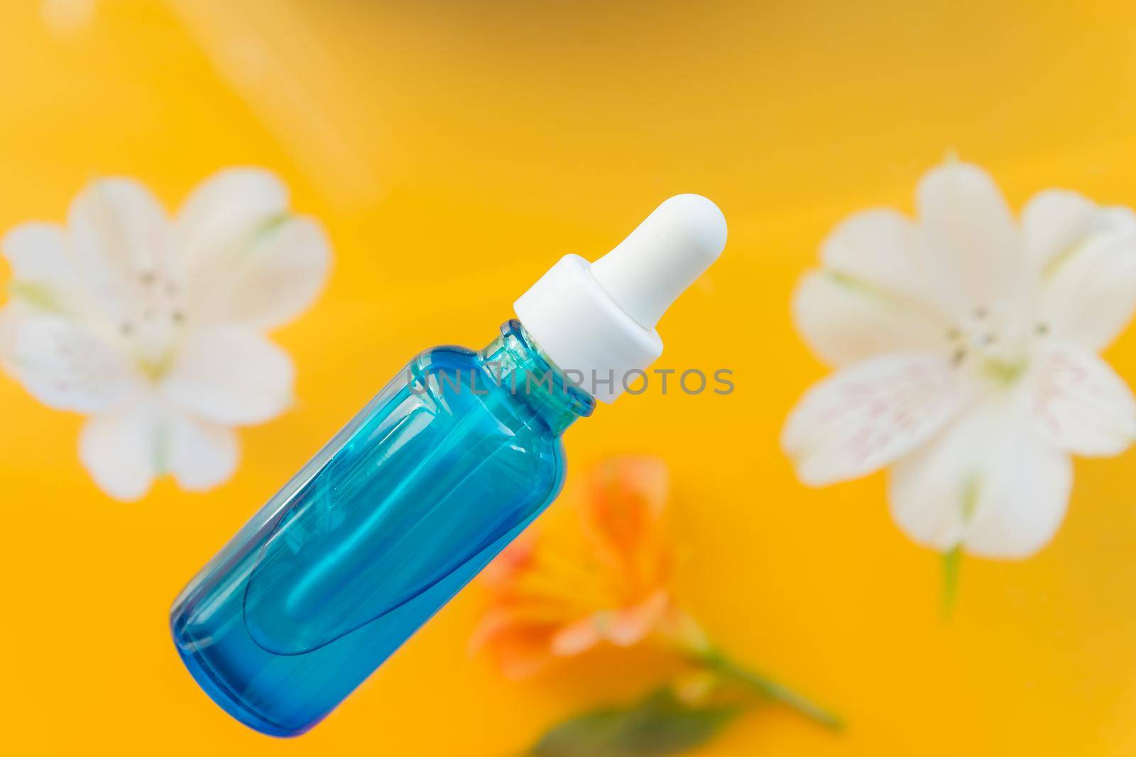 Serum glass bottle with pipette and beautiful flowers on the beige gold background. Natural organic spa cosmetic concept.