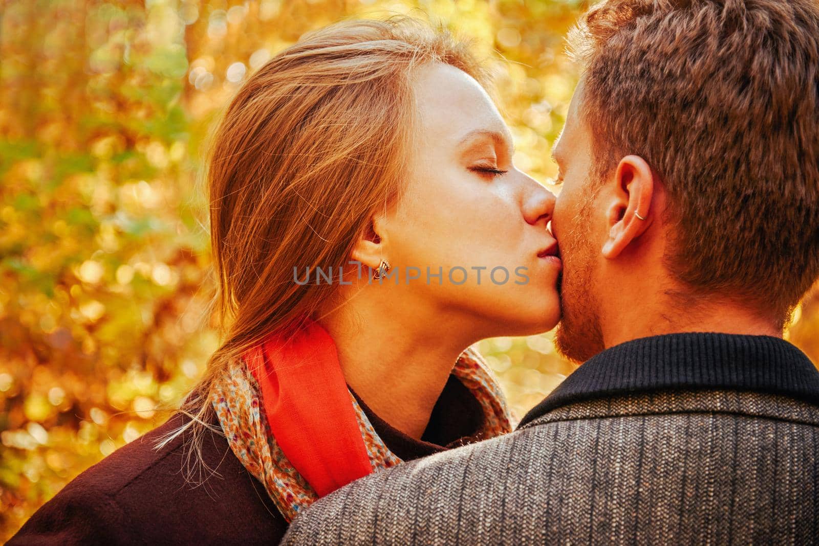 Young beautiful woman with closed eyes kissing a man in autumn park