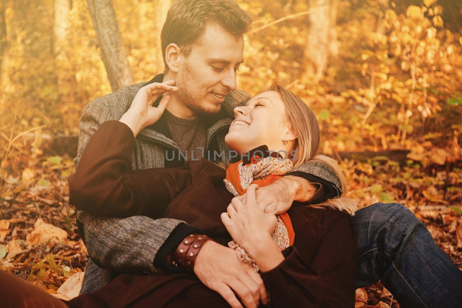 Young loving couple rests in autumn park, man embraces a woman. Image with sunlight effect.