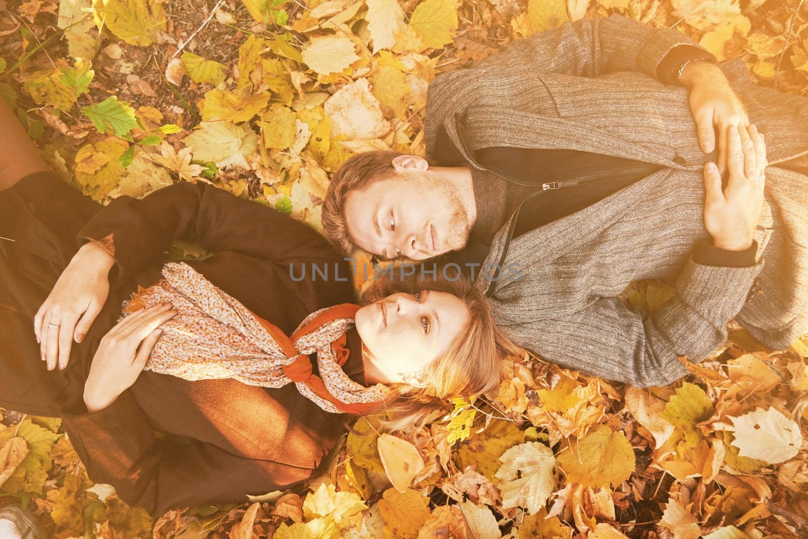 Loving couple lying on autumn leaves in the park. Image with sunlight effect.