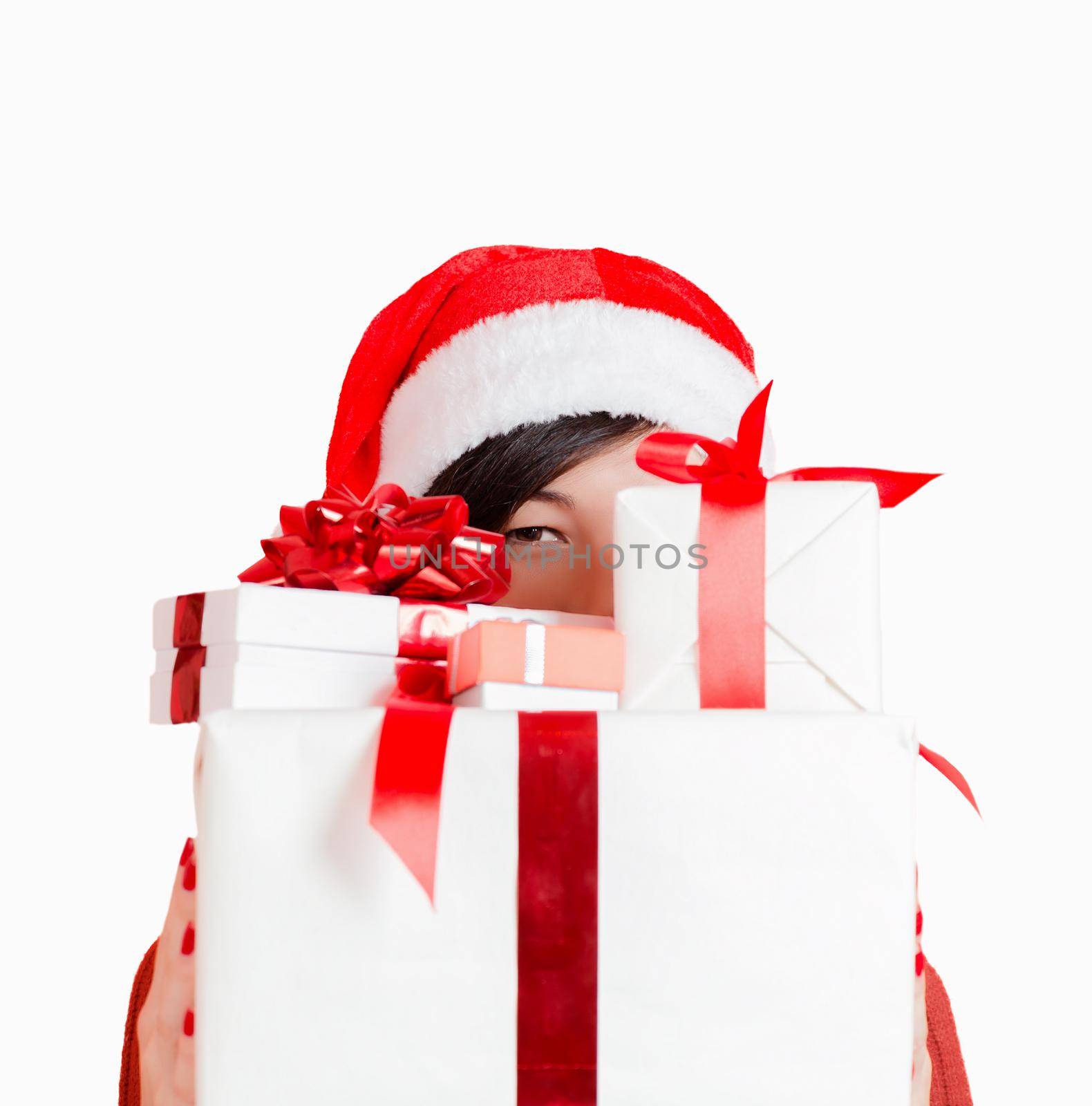 Young woman in santa hat looks out from behind gift box on a white background