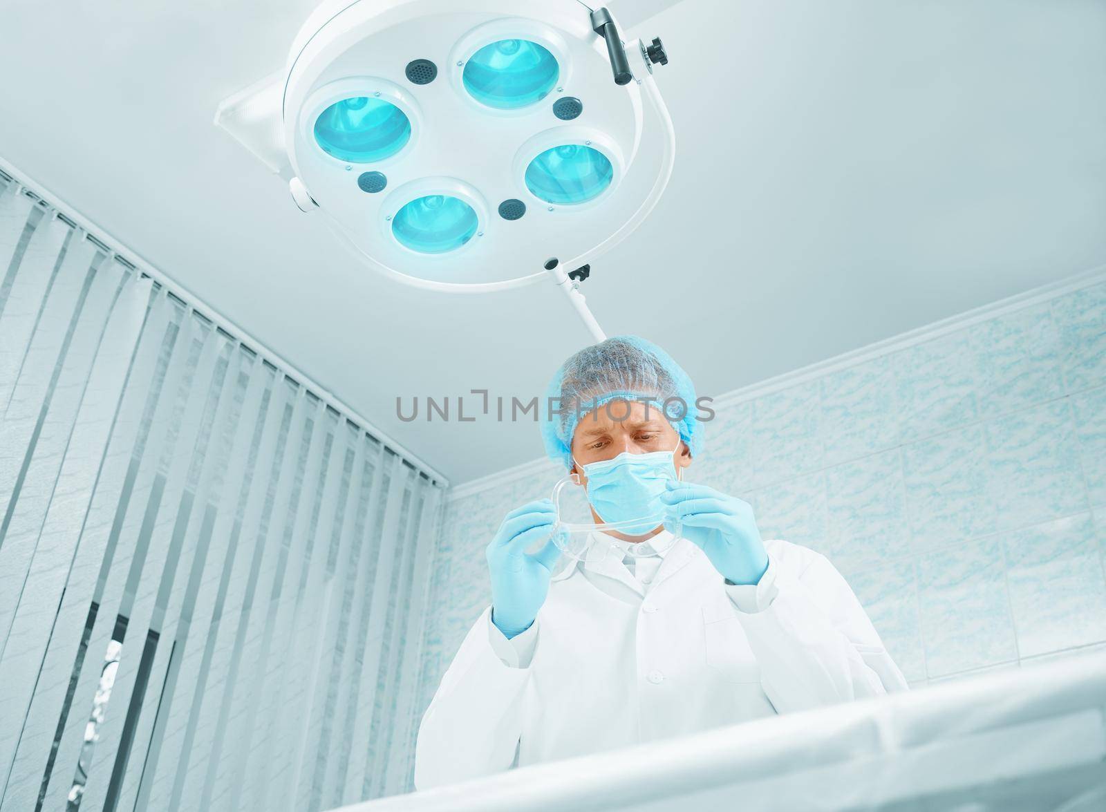 Young man surgeon takes off his protective glasses after operation