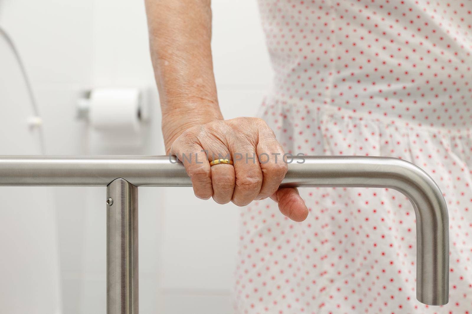 Elderly woman holding on handrail in toilet.