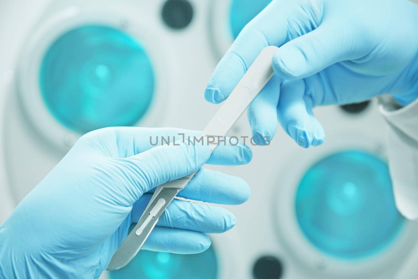 Assistant passes a scalpel to surgeon on operation on background of surgical lamp, view of hands