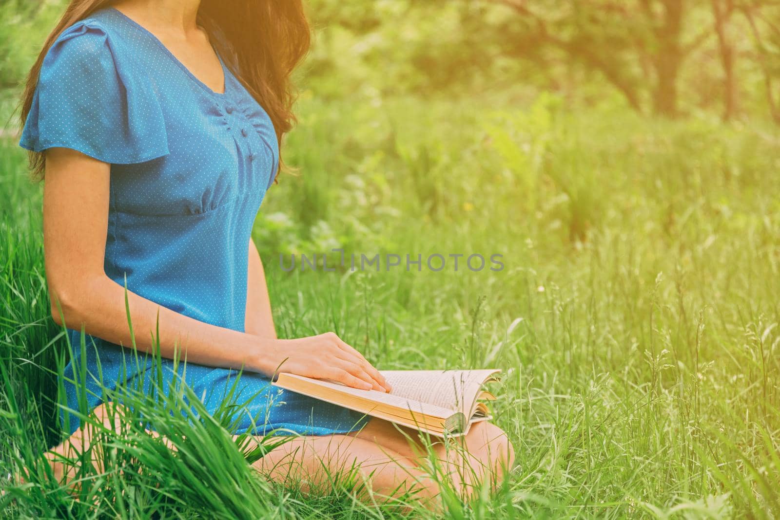 Unrecognizable girl reading book in summer park outdoor. Image with sunlight effect