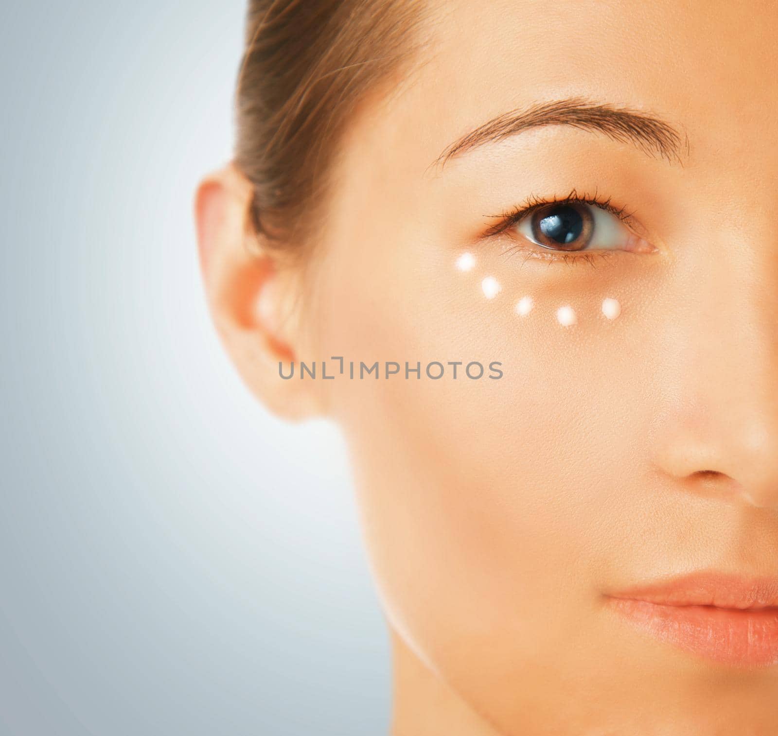 Portrait of a beautiful young woman, a cream applied around the eye, concept of skincare